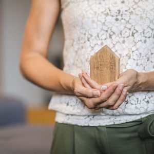 Frau hält ein kleines Haus aus Holz mit der Aufschrift Welcome Home in Händen