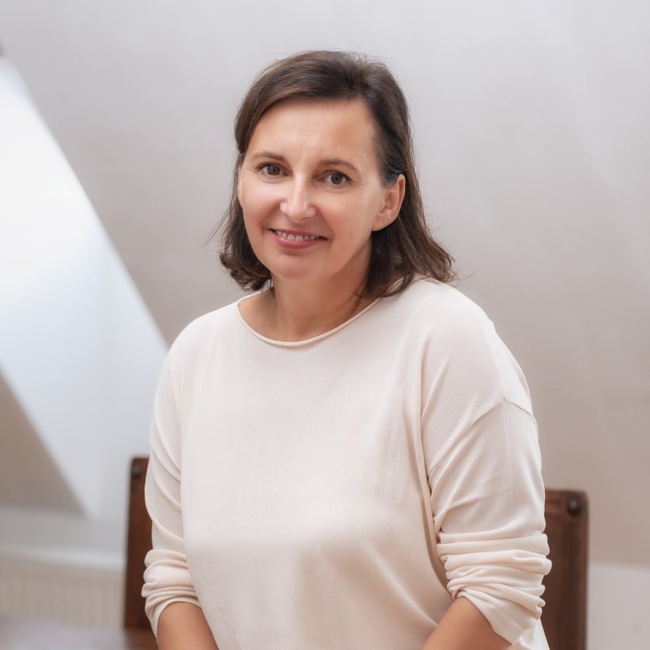 Andrea Auer Eine Frau mit weißem Pullover sitzt auf einem Holzstuhl