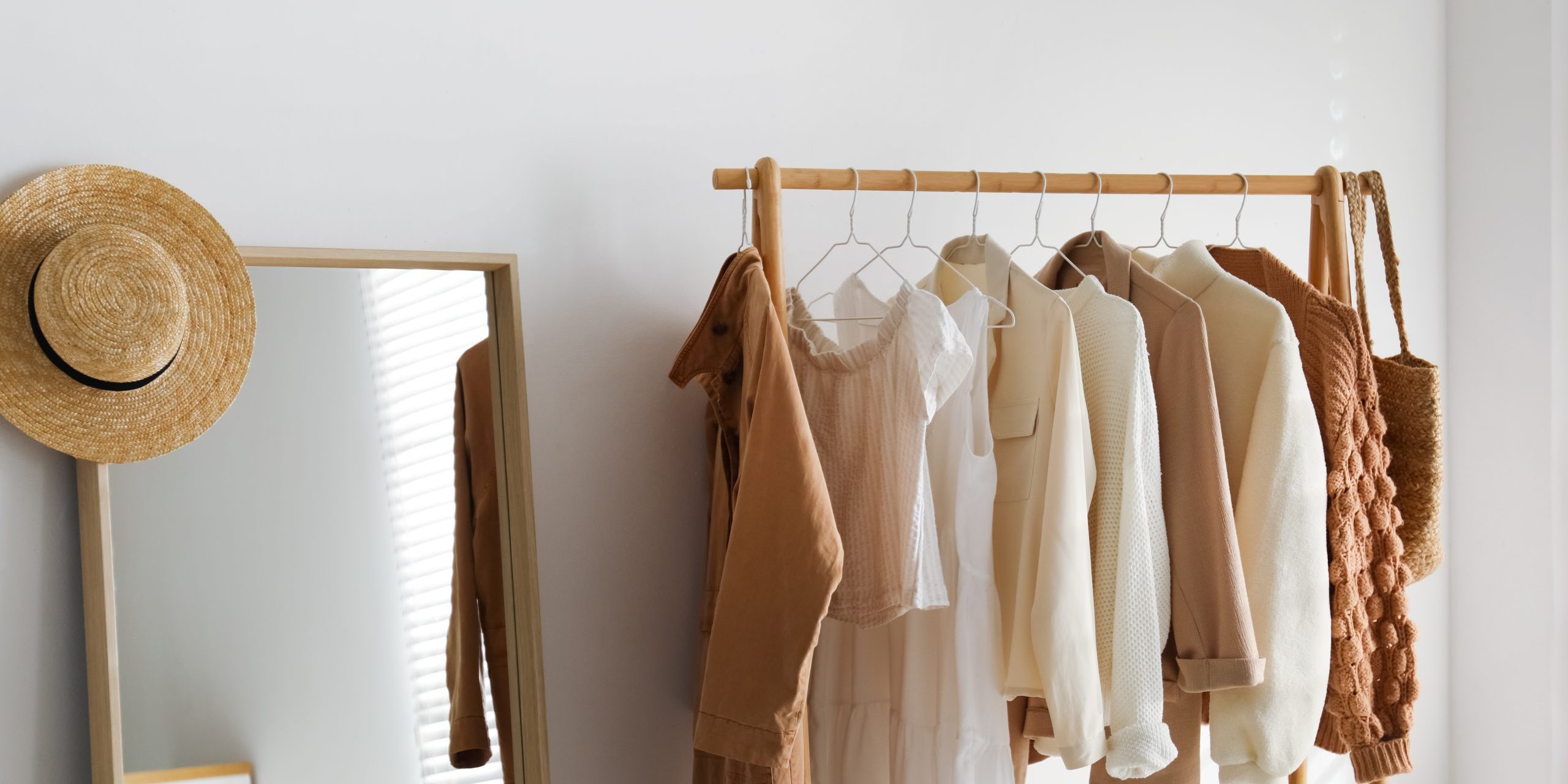 Rack with stylish women's clothes in dressing room. Modern interior design Bild von einer Kleiderstange mit Bekleidung und daneben ein Spiegel auf dem ein Hut hängt