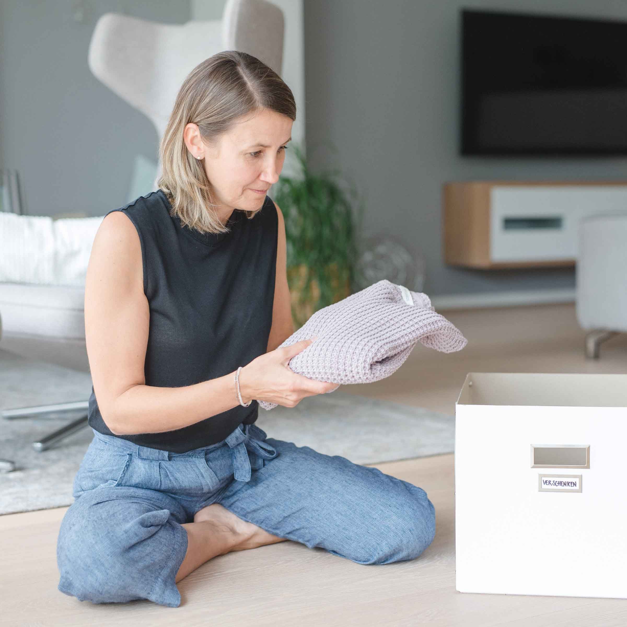 Frau die einen Pullover in der Hand hält um ihn in eine Box zu legen.
